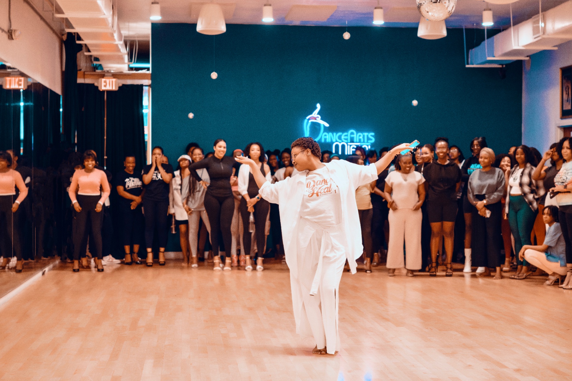Sephora leading a Dance & Heal workshop, arms outstretched, surrounded by participants at DanceArts Miami.